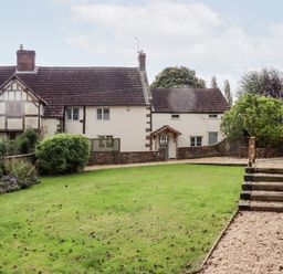 A garden with grass lawn and gravel path in front of a traditional cottage at 1 White House Cottages Bromsash near Lea