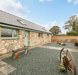 An exterior view of a stone house with green window frames and door a gravel yard with rustic bench and metal wheel at Y Felin The Granary in Caernarfon