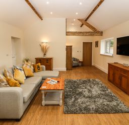 A living room with a gray sofa and cushions a wooden coffee table a gray rug a wooden cabinet and a wall mounted TV at Y Felin The Granary in Caernarfon