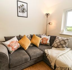 A corner sofa with cushions and a blanket next to a window in a living room at Ty Gwair The Hayloft in Caernarfon