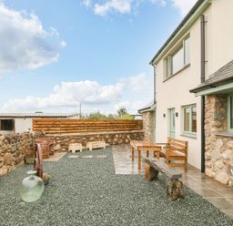 An outdoor patio area with wooden bench and table stone walls and gravel ground at Ty Gwair The Hayloft in Caernarfon