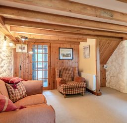A sitting room with a sofa, an armchair, wooden ceiling beams, and a stone wall at Tryfan Cottage in Rhostryfan near Caernarfon