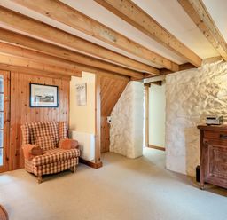 A living room with wooden beams on the ceiling a plaid armchair a wooden cabinet and stone walls at Tryfan Cottage in Rhostryfan near Caernarfon