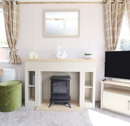 A living room with a fireplace, a television, and windows with plaid curtains at 25 Sherwood in South Lakeland Leisure Village