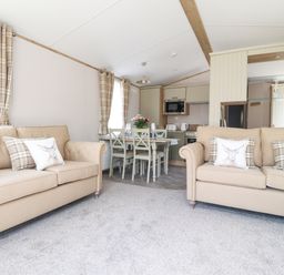 A living area with two beige sofas and a dining table with chairs and a kitchen in the background at 25 Sherwood South Lakeland Leisure Village
