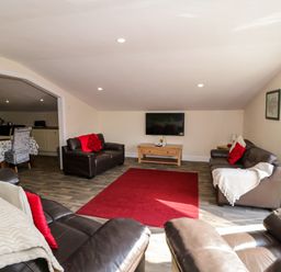 A living room with brown leather sofas a red rug and a wall-mounted TV at The Apartment at Plas Yr Eithin in Amlwch near Llanfechell