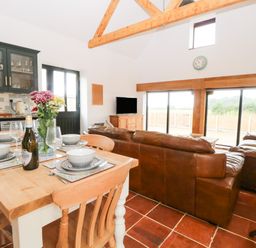 An open plan kitchen dining and living area with wooden table and chairs leather sofas and large sliding glass doors at Little Barn in Tittleshall