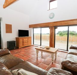 A living room with leather sofas a wooden coffee table a TV on a wooden cabinet and large windows at Little Barn in Tittleshall