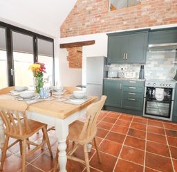 A kitchen with wooden dining table and chairs and green cabinets at Little Barn in Tittleshall