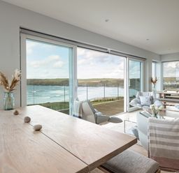 A dining table with vases and stones next to a sitting area with chairs and windows showing a sea view at Seascape in Polzeath