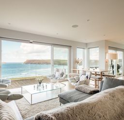 A living room with chairs a glass coffee table a dining table a floor lamp and a telescope with an ocean view at Seascape in Polzeath