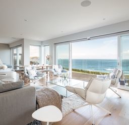 A living room with armchairs a glass coffee table and large windows overlooking the ocean at Seascape in Polzeath