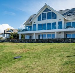 A two story house with large windows and a glass balcony on a grassy hill at Seascape in Polzeath