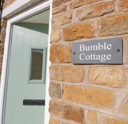 A green front door and a wall with a sign that says Bumble Cottage at Bumble Cottage in Tysoe