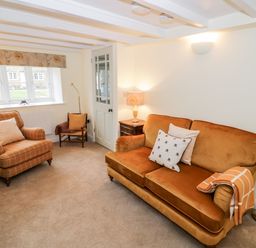 A living room with a sofa armchair small chair side table lamps and a window at Bumble Cottage in Tysoe
