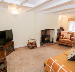 A living room with a wood burning stove armchairs a television and a basket of firewood at Bumble Cottage in Tysoe