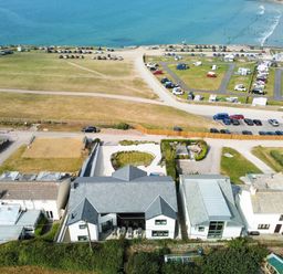 Aerial view of houses near a beach with cars parked on roads and grassy areas at Megizzy in Polzeath
