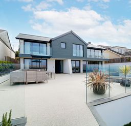 A modern two-story house with glass balcony railings and outdoor seating area at Megizzy in Polzeath
