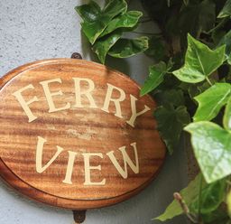 A wooden sign with the words Ferry View surrounded by green leaves
