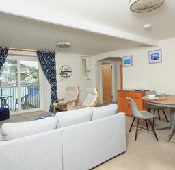 A living room with a sofa two armchairs a round dining table with chairs and a balcony with water view at Ferry View Dartmouth