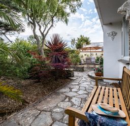 An outdoor patio with a wooden bench stone pathway garden plants and a table with chairs under an umbrella at Longhouse Bungalow in Rock