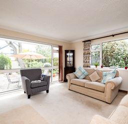 A sitting room with beige sofas blue cushions and a striped armchair near large windows at Longhouse Bungalow in Rock
