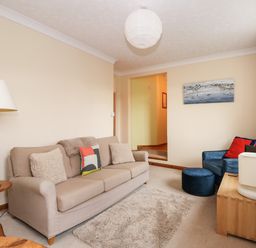 A living room with a beige sofa and a blue armchair with cushions at 16 Norfolk Heights in Docking