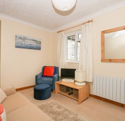 A sitting room with a beige sofa and blue armchair near a window with curtains and a wooden TV stand at 16 Norfolk Heights Docking