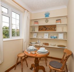 A dining area with a small round wooden table set for two and wooden chairs near shelves with decorative items at 16 Norfolk Heights in Docking