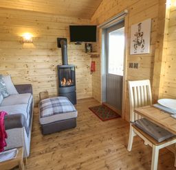 A wooden living room with a sofa ottoman wood stove dining table and chair at Foxes Den in Winston near Staindrop