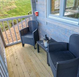A small wooden balcony with two black wicker chairs and a table holding a bottle in a metal bucket and two glasses at Foxes Den in Winston near Staindrop
