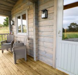 A wooden porch with two chairs a table and a glass door at Otters Holt in Winston near Staindrop