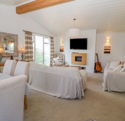 A living room with sofas chairs a guitar and a television mounted on a wall at Sunstone Lodge Garreg Haul Lodge Cilan near Abersoch