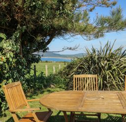 An outdoor dining area with a table and chairs overlooking the sea at Sunstone Lodge (Garreg Haul Lodge) Cilan near Abersoch