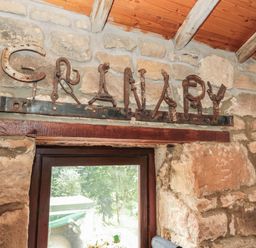 A stone wall with a wooden beam above a window and metal letters spelling granary at The Granary in Rothbury