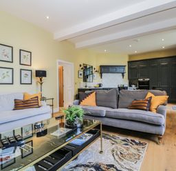 A living room with two sofas and a glass coffee table next to an open kitchen with dark cabinets at Tarn End Cottages 5 Talkin near Brampton Cumbria