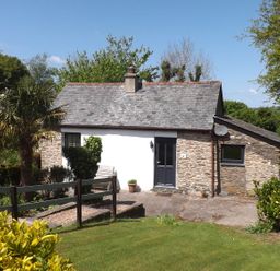A small stone cottage with a gray door and chimney surrounded by trees and lawn at Beech Cottage in Combe Martin