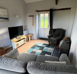 A living room with a grey sofa a grey armchair a TV on a stand a wood burning stove and a patterned rug at Beech Cottage in Combe Martin