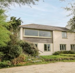 A building with multiple windows surrounded by trees and shrubs at Porth Farm Annexe in Mawgan Porth