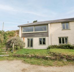 Exterior view of a two-story house with stone steps and greenery at Porth Farm Annexe in Mawgan Porth