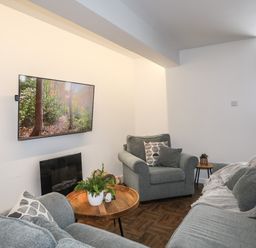 A living room with grey sofas a wooden coffee table a wall-mounted tv and plants at Y Goedwig in Newborough