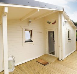 An exterior view of a small building with wooden decking a door two windows wall lamps and decorative butterflies at Port Heron Lodge Ballykeeran near Glasson County Westmeath