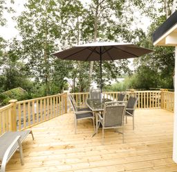 An outdoor wooden deck with a glass table and six chairs under a large umbrella near trees at Port Heron Lodge Ballykeeran near Glasson County Westmeath