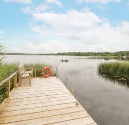 A wooden dock with a bench and a lifebuoy overlooking a lake with two people canoeing at Port Heron Lodge in Ballykeeran near Glasson County Westmeath
