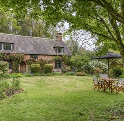 A stone cottage with a garden lawn and outdoor table with chairs under a tree at Saint Pancras Chapel in Washford near Williton
