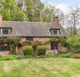 A stone cottage with a tiled roof two chimneys and trimmed bushes in front at Saint Pancras Chapel in Washford near Williton