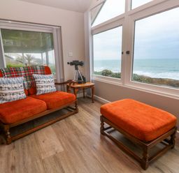 A living room with a sofa, telescope and large windows at Stonecroft in Praa Sands