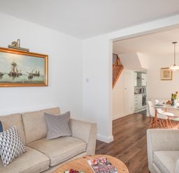 A living room with beige sofas and pillows and a painting on the wall next to a dining area with a table and chairs at The Shambles in Fortuneswell