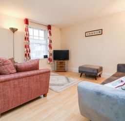 A living room with red and gray sofas a television on a stand a floor lamp and floral curtains at 1 Tregonwell Court in Minehead