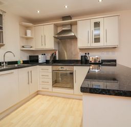 A kitchen with white cabinets black countertops a stainless steel oven and extractor fan at 1 Tregonwell Court Minehead